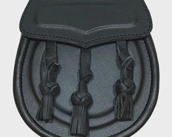 Può includere: Sporran in pelle nera con patta superiore e tre nappe decorative. Lo sporran ha un fondo arrotondato ed è disegnato con una serie di cerchi concentrici. La patta è cucita lungo il bordo superiore.