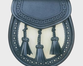 May include: A black leather sporran with a white fur front and three black tassels. The sporran has decorative stitching and a flap with a scalloped edge. The design is a traditional Scottish accessory.