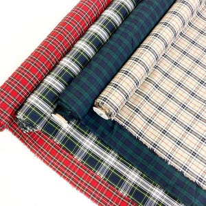 May include: Several rolls of plaid fabric in various colors, including red, green, navy, and beige. The fabric is rolled up, showcasing the different patterns and colors. The plaid designs feature intersecting lines in a classic tartan style.