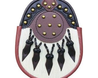 Può includere: Un tradizionale sporran, un accessorio dell'abbigliamento delle Highlands scozzesi. Lo sporran presenta una parte superiore in pelle marrone con borchie in ottone, un corpo in pelliccia bianca e cinque nappe in pelle. I bordi sono rifiniti in pelle rossa.