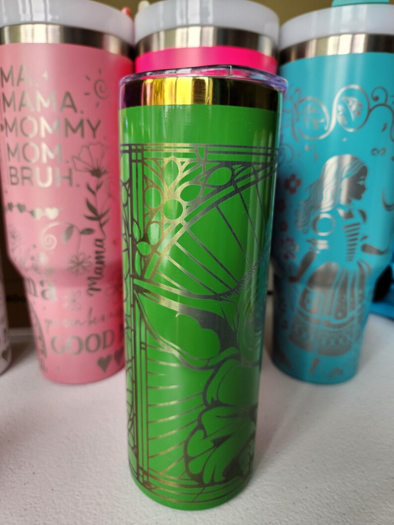 May include: A collection of insulated tumblers in various colors. The central tumbler is green with a gold floral design. Other tumblers are pink and teal, with white lids and various text and graphic designs.