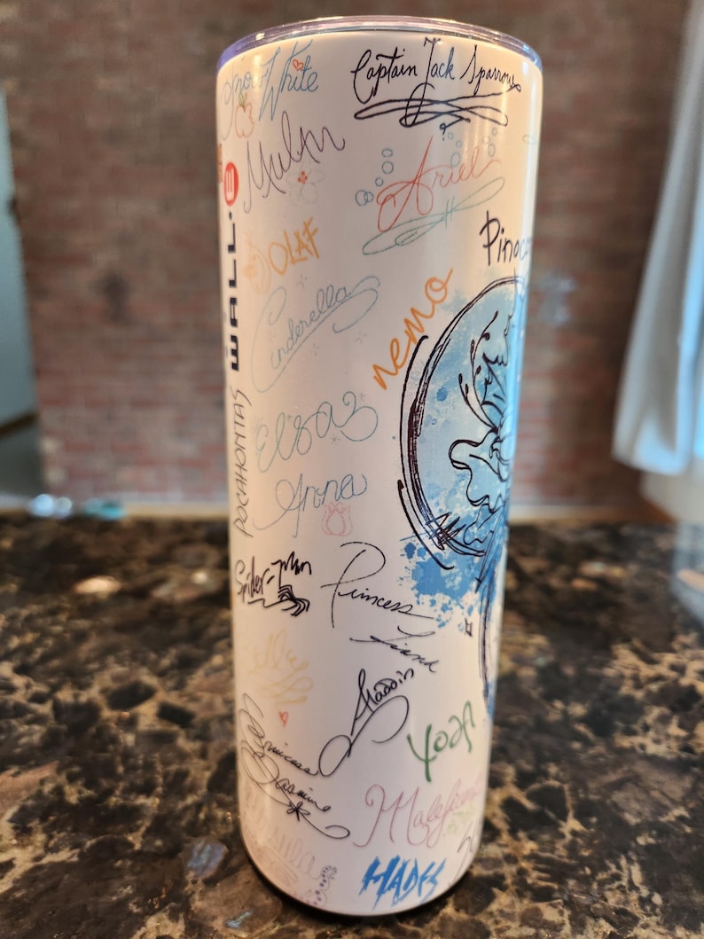 May include: A white insulated tumbler with signatures of characters like Olaf, Cinderella, and Ariel in various colours. The tumbler has a blue and white design and is suitable for hot and cold drinks.