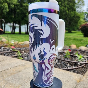 Peut inclure: Un grand gobelet cylindrique en acier inoxydable avec une poignée blanche et un couvercle transparent. L'extérieur présente une finition métallique irisée avec un motif blanc représentant une silhouette stylisée à cornes et des motifs fluides.