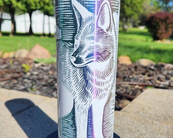 Puede incluir: Un vaso de acero inoxidable blanco con una ilustración detallada de un zorro. El diseño del zorro es en tonos de blanco, azul, morado y verde. El borde superior del vaso tiene un acabado brillante e iridiscente.