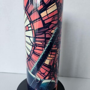 Puede incluir: Un vaso alto y aislado con un dise&ntilde;o de vidriera en tonos rojos, naranjas y negros. El vaso tiene una tapa transparente y una base negra. El dise&ntilde;o presenta formas y l&iacute;neas geom&eacute;tricas.