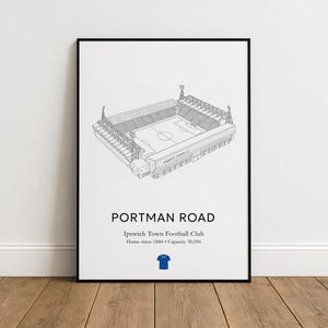 May include: Black framed print of Portman Road stadium, home of Ipswich Town Football Club. The stadium is depicted in a detailed line drawing. Text includes "Portman Road", team details, and a blue jersey icon. Capacity 30,056.
