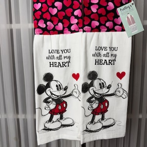 May include: Two white kitchen towels with a black and red heart pattern at the top. The towels feature Mickey Mouse illustrations and the text "LOVE YOU with all my HEART". A tag from "Kathy's Kitchen Boa" is attached.