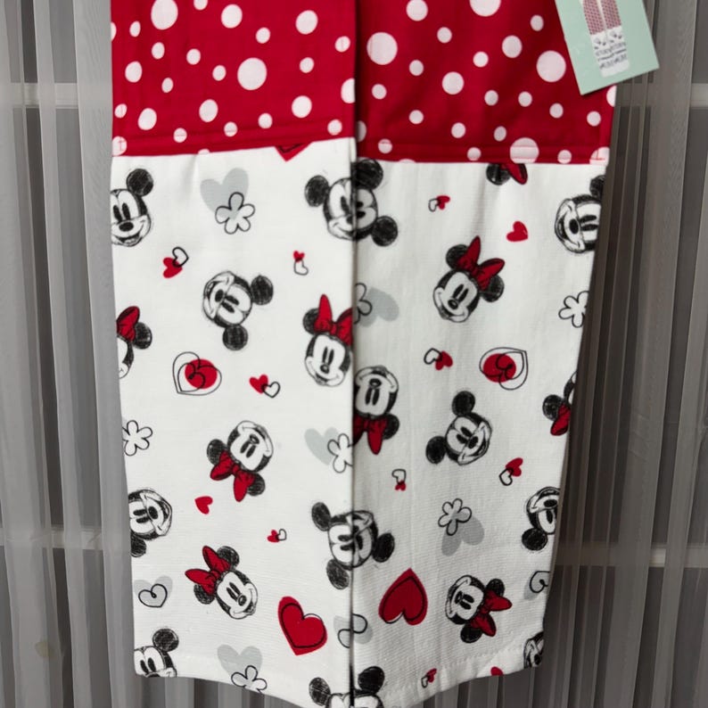 May include: A red and white polka dot and Minnie Mouse patterned kitchen towel. The top section is red with white polka dots. The bottom section is white with Minnie Mouse, hearts, and flower graphics.