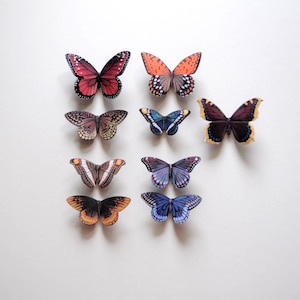 May include: An assortment of colorful butterfly decorations with intricate wing patterns. The butterflies are in various sizes and colors, including red, orange, brown, blue, and purple, against a white background.