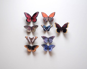 May include: An assortment of colorful butterfly decorations with intricate wing patterns. The butterflies are in various sizes and colors, including red, orange, brown, blue, and purple, against a white background.