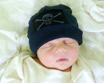 May include: A sleeping baby wearing a dark blue beanie with a white skull and crossbones design.