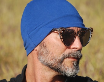 May include: A person wearing a royal blue beanie and leopard print heart-shaped sunglasses. The beanie is made of a soft, stretchy fabric.