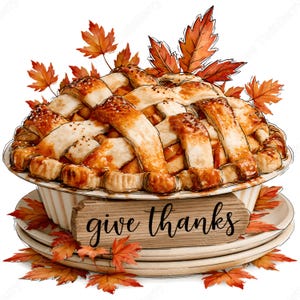 May include: A baked fruit pie with a golden-brown lattice crust, resting on a stack of two white plates. A wooden sign with the text "give thanks" is attached to the front. The entire arrangement is surrounded by scattered orange and red maple leaves.