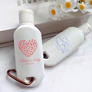 May include: Two white, travel-sized bottles with flip-top lids. One bottle features a heart design made of small red hearts, with the names "Michael & Emily" and the date "03.14.2025" printed in red. The other bottle has the same names and date in blue.