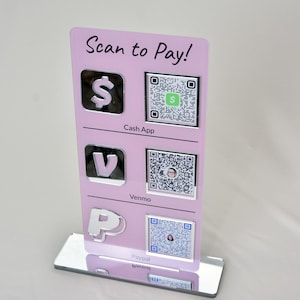 May include: A pink acrylic sign with the text "Scan to Pay!" and payment app logos for Cash App, Venmo, and Paypal. Each app has a corresponding QR code for easy payment. The sign has a mirrored base.