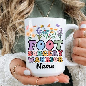 Könnte beinhalten: Weiße Keramik-Tasse mit dem Schriftzug "FOOT SURGERY WARRIOR" in farbenfrohen Retro-Buchstaben, umgeben von floralen und Insekten-Illustrationen. Das Wort "Name" steht unter dem Text und ist zur Personalisierung bereit.