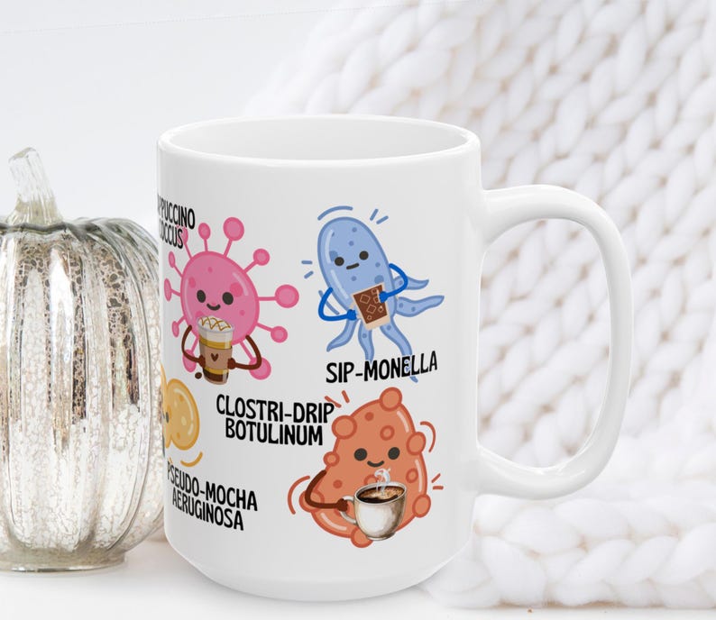May include: White ceramic coffee mug featuring cartoon illustrations of microbes with coffee-themed puns. The mug includes the phrases "Cappuccino Coccus", "Sip-Monella", "Clostri-Drip Botulinum", and "Pseudo-Mocha Aeruginosa".