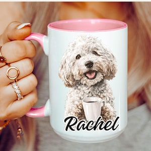 May include: A white ceramic mug with a pink interior and handle. The mug features a watercolor illustration of a fluffy white dog with a coffee cup and the name "Rachel" in black script. The mug is held by a person.