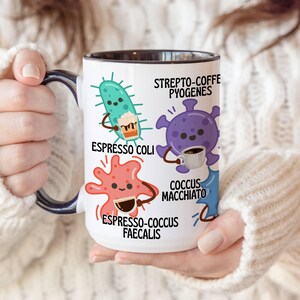 May include: White ceramic coffee mug with a black interior and handle, featuring cartoon illustrations of bacteria holding coffee cups. Text includes "Espresso Coli," "Strepto-Coffe Pyogenes," "Coccus Macchiato," and "Espresso-Coccus Faecalis."
