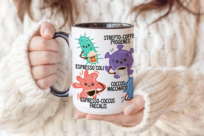 May include: White ceramic coffee mug with a black interior and handle, featuring cartoon illustrations of bacteria holding coffee cups. Text includes "Espresso Coli," "Strepto-Coffe Pyogenes," "Coccus Macchiato," and "Espresso-Coccus Faecalis."