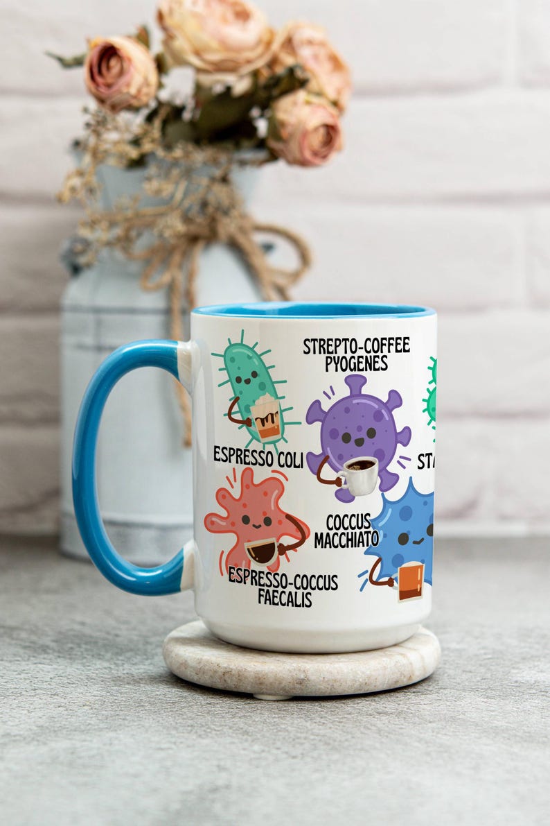 May include: White ceramic mug with a blue interior and handle. The mug features cartoon illustrations of bacteria, each holding a coffee cup or espresso. Text includes "Strepto-Coffee Pyogenes" and "Espresso Coli".