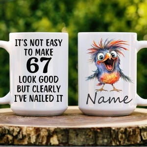 May include: A white ceramic mug featuring the black text IT'S NOT EASY TO MAKE 67 LOOK GOOD BUT CLEARLY I'VE NAILED IT on one side and a colorful, spiky-haired cartoon bird illustration with the word Name printed in black script on the other side.