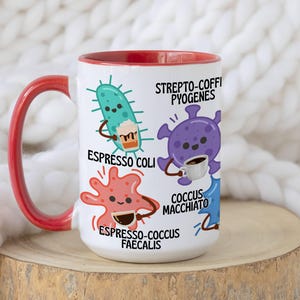 May include: White ceramic coffee mug with a red interior and handle. The mug features cartoon illustrations of microbes with coffee cups and the phrases "Espresso Coli," "Strepto-Coffi Pyogenes," and "Espresso-cocus Faecalis."