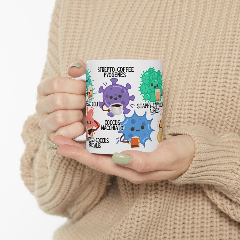 May include: White ceramic mug featuring cartoon illustrations of bacteria, each with a coffee-related pun. The mug includes the text "STREPTO-COFFEE PYOGENES," "COCCUS MACCHIATO," and other similar puns. The design incorporates various colors and shapes.