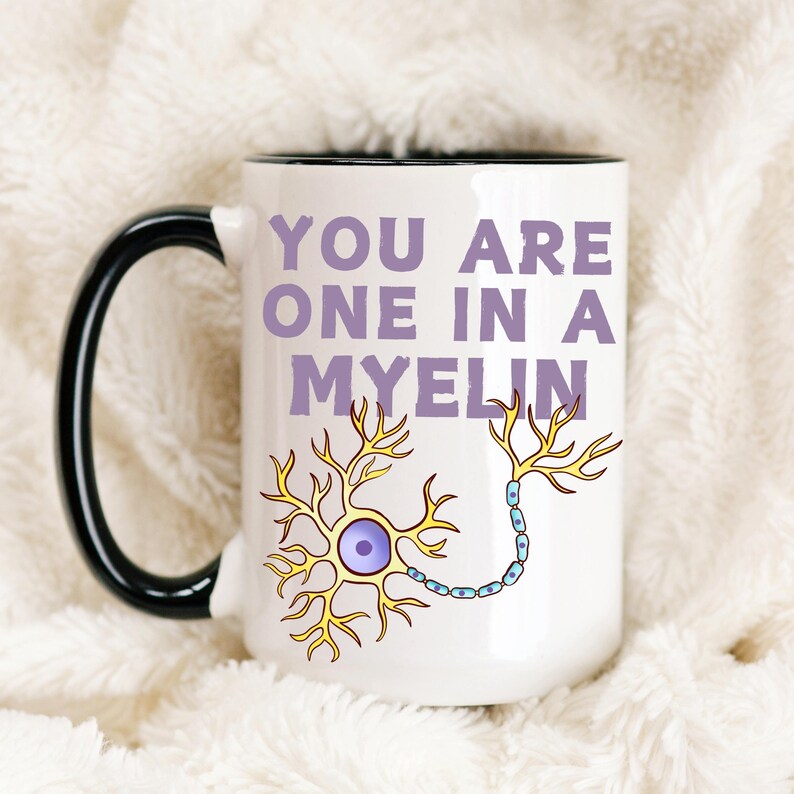 May include: White ceramic mug with a black handle and rim. The mug features the text "YOU ARE ONE IN A MYELIN" in purple, along with a yellow and blue neuron illustration. The mug is set against a soft, white background.