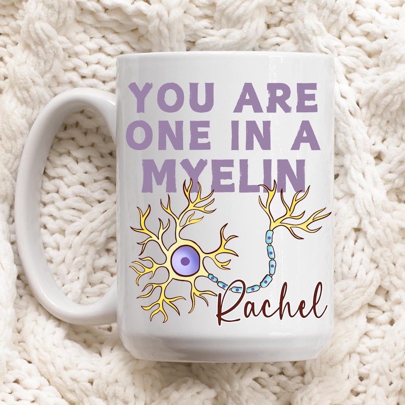May include: White ceramic mug featuring the text "YOU ARE ONE IN A MYELIN" in purple, and a neuron illustration in yellow and blue. The name "Rachel" is written in a cursive font. A great gift for a science lover.