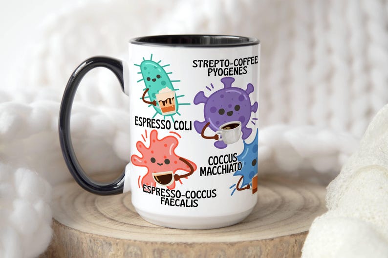 May include: White ceramic coffee mug with a black handle and rim. The mug features cartoon illustrations of bacteria, each holding a coffee cup. Text includes "Espresso Coli," "Strepto-Coffee Pyogenes," "Espresso-Cocus Faecalis," and "Cocus Macchiato."