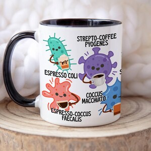 May include: White ceramic mug with a black handle and rim, featuring cartoon illustrations of bacteria holding coffee cups. Text includes "Strepto-Coffee Pyogenes," "Espresso Coli," and "Espresso-Cocus Faecalis."