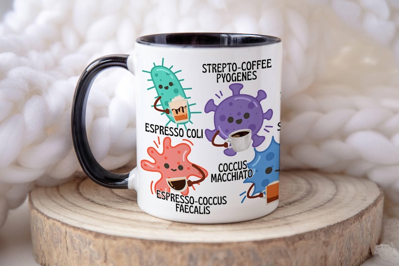 May include: White ceramic mug with a black handle and rim, featuring cartoon illustrations of bacteria holding coffee cups. Text includes "Strepto-Coffee Pyogenes," "Espresso Coli," and "Espresso-Cocus Faecalis."