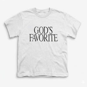 以下が含まれることがあります： 「GOD'S FAVORITE」の黒い文字がプリントされた、白い半袖Tシャツ。クルーネックのTシャツはシンプルなデザインで、普段使いに適しています。