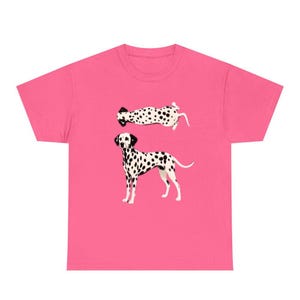 May include: A bright pink short-sleeved t-shirt featuring a graphic print of two Dalmatian dogs. One dog is depicted standing in profile, while the other is shown lying down in a horizontal position. Both dogs have white coats with black spots.
