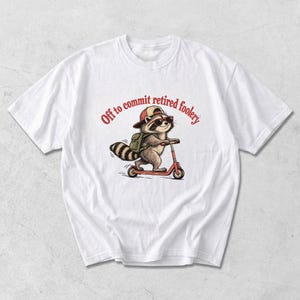 Könnte beinhalten: Ein weißes Kurzarm-T-Shirt mit einer Grafik eines Waschbären, der eine rote Baseballkappe und eine Sonnenbrille trägt, einen grünen Rucksack aufhat und auf einem roten Roller fährt. Der Text "Off to commit retired foolery" steht in Rot darüber.