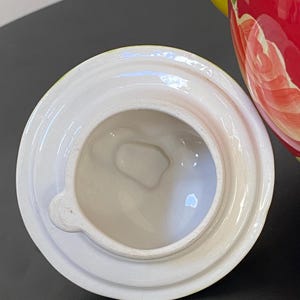 以下が含まれることがあります： 白いセラミックティーポットの蓋、取っ手付き。 蓋は丸く、縁が盛り上がっており、中央に開口部があります。 ティーポット本体は赤色で、花柄と黄色のアクセントが施されています。