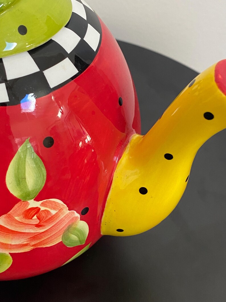 以下が含まれることがあります： カラフルな陶器のティーポット。赤いボディに花柄、黒い水玉模様の黄色の注ぎ口、白と黒の市松模様の緑色の蓋が特徴です。装飾的なキッチンアイテムです。