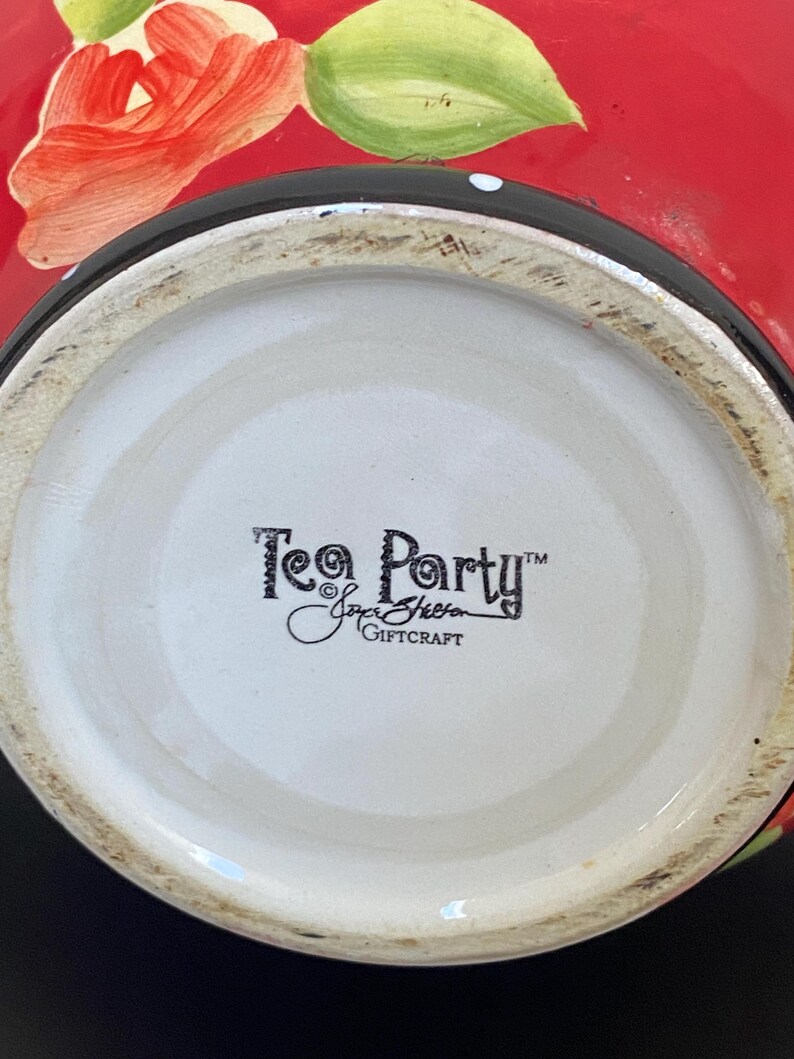 以下が含まれることがあります： 赤色の外側、黒い縁、白い内側を持つセラミックティーパーティーボウル。ボウルには手描きの赤いバラと緑の葉が描かれています。ボウルの底には「Tea Party」と「Joyce Sheen Giftcraft」の文字があります。