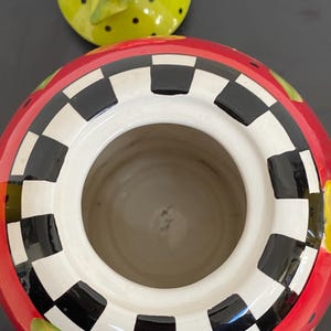 以下が含まれることがあります： 赤色の外観、白と黒の市松模様の縁、白い内側のセラミック容器。 蓋はライムグリーンで黒い水玉模様と赤いバラが付いています。 この容器は、キッチンや家の装飾用である可能性があります。