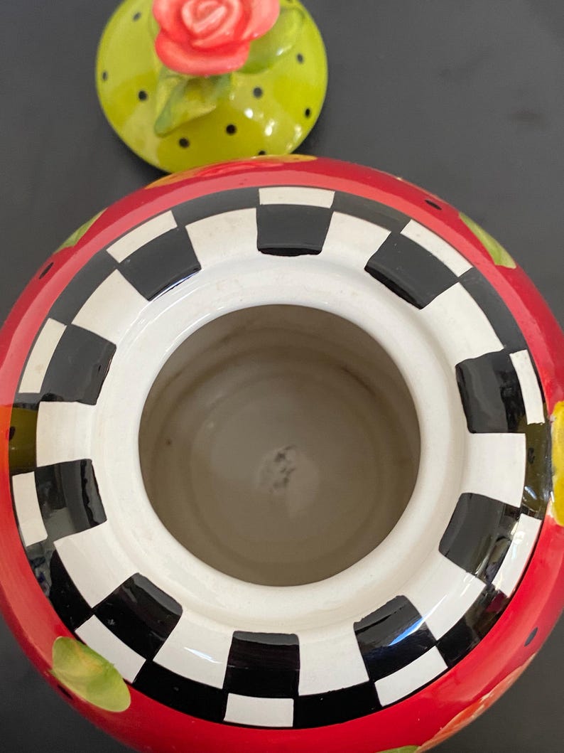 以下が含まれることがあります： 赤色の外観、白と黒の市松模様の縁、白い内側のセラミック容器。 蓋はライムグリーンで黒い水玉模様と赤いバラが付いています。 この容器は、キッチンや家の装飾用である可能性があります。
