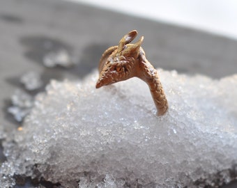 May include: A gold-colored ring with a detailed dragon design. The ring is partially submerged in a bed of white, sparkly crystals.