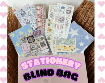 May include: A pink paper bag labeled "STATIONERY BLIND BAG" filled with various stationery items. The bag contains sticker sheets, washi tape, and small notebooks with colorful illustrations and designs. The background includes decorative hearts.