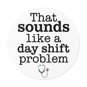 May include: A circular white sticker featuring the black text "That sounds like a day shift problem" in a bold, serif font. Below the text is a small, simple illustration of a medical stethoscope with blue tubing and a silver chest piece.