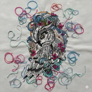 May include: Embroidered owl design in shades of gray, white, and pink, with blue accents and floral details. The owl is surrounded by loose threads in various colors, creating a handcrafted aesthetic. The artwork is on a white fabric.