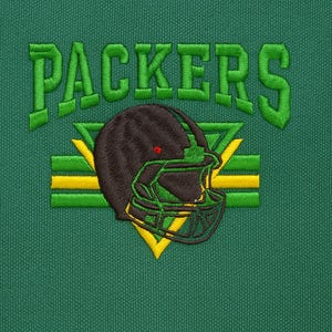 Op de afbeelding: Groene stof met een geborduurd ontwerp met het woord "PACKERS" in groen, boven een footballhelm. De helm is bruin en groen, met gele accenten. De achtergrond is effen groen.