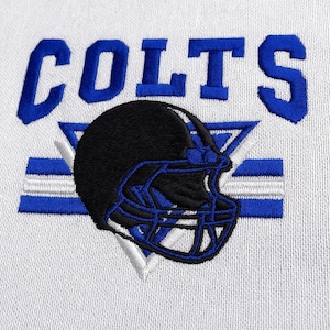 May include: White fabric with an embroidered design featuring the word "COLTS" in blue, above a black and blue football helmet. The helmet is centered over blue and white horizontal stripes.