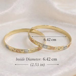 Può includere: Due braccialetti dorati con un motivo floreale in oro rosa, giallo e bianco. Il diametro interno di ogni braccialetto è di 6,42 cm. I braccialetti sono esposti su una superficie color crema.