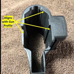 Op de afbeelding: Een zwart, 3D-geprint object met een holle binnenkant en een rechthoekige vorm. De tekst "Aligns with Gun Profile" is zichtbaar. Het object lijkt ontworpen om in een specifiek profiel te passen.