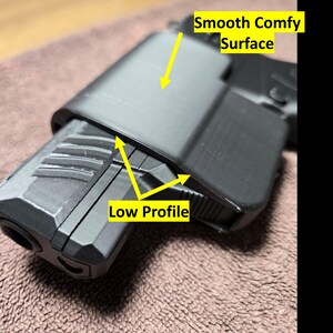 May include: A black, low-profile object with a smooth, comfy surface. The object is resting on a brown, textured surface. The text "Smooth Comfy Surface" and "Low Profile" are visible.